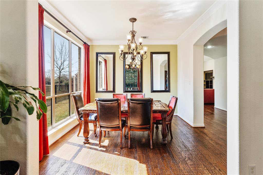 The formal dining room is a stunning space featuring gleaming hardwood floors and exquisite crown molding, creating an atmosphere of timeless elegance. A wall of windows floods the room with natural light, enhancing its inviting and airy feel.