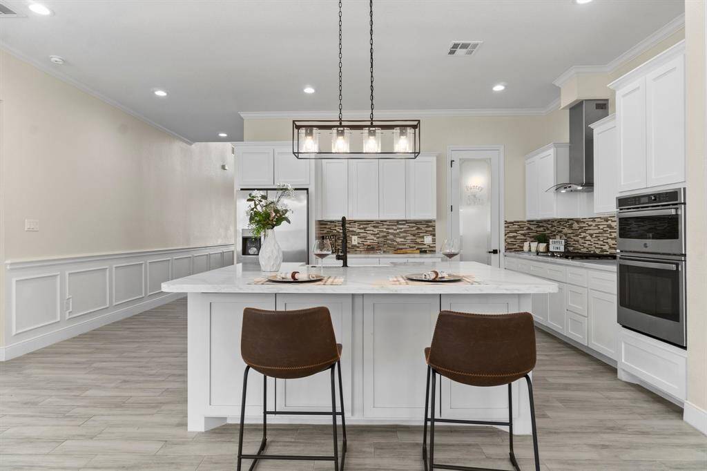 This modern kitchen features sleek white cabinetry, a spacious island with seating, and contemporary light fixtures. It boasts stainless steel appliances, a stylish backsplash, and ample space for dining and entertaining. The neutral color palette and open layout create an inviting atmosphere.