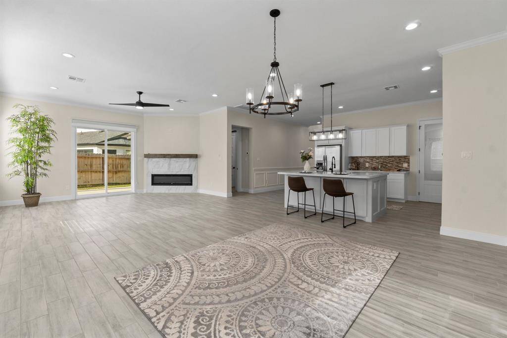 This open-concept living area features modern flooring, a cozy mock fireplace, and ample natural light from large sliding doors to the backyard. The spacious kitchen includes a stylish island with seating, pendant lighting, and contemporary finishes, perfect for entertaining.