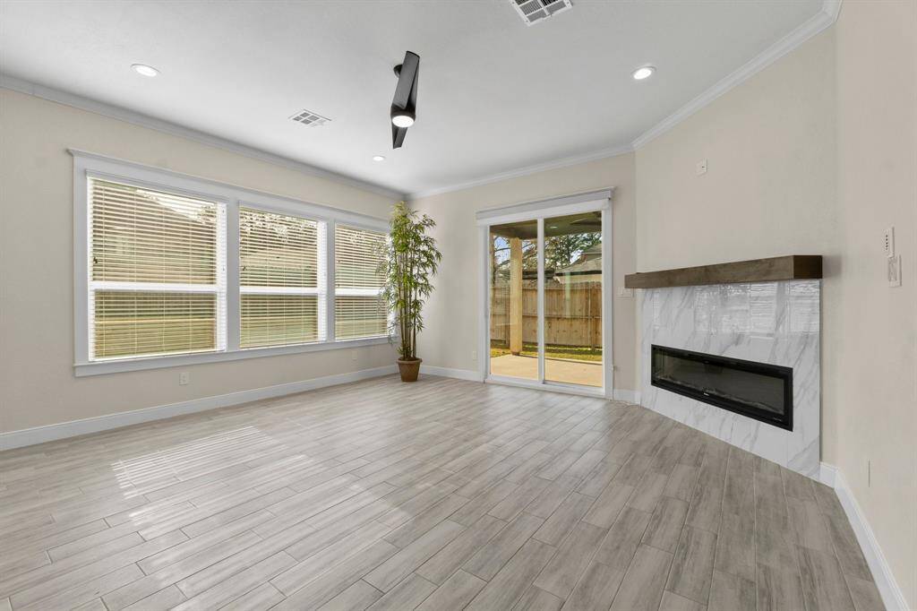 This bright living area features large windows, a mock fireplace with a sleek mantel, and sliding glass doors leading to a fenced backyard. The light wood-style flooring and neutral walls create a spacious and inviting atmosphere.