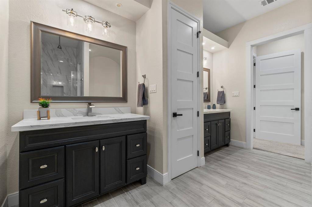 The primary bathroom features a modern design with dual vanities, sleek dark cabinetry, and a spacious layout. It includes stylish fixtures, large mirrors, and neutral tile flooring, offering both functionality and elegance.