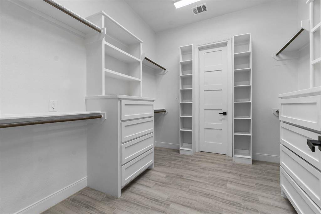Spacious walk-in closet in the primary bedroom, with ample shelving, hanging rods, and drawers. Features a modern design with white cabinetry and light wood flooring, offering plenty of storage and organization options.