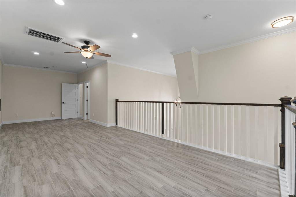 This photo shows a bright, open loft area with light wood flooring and neutral walls. It features recessed lighting, a ceiling fan, and a railing overlooking the floor below, providing a versatile space for various uses.