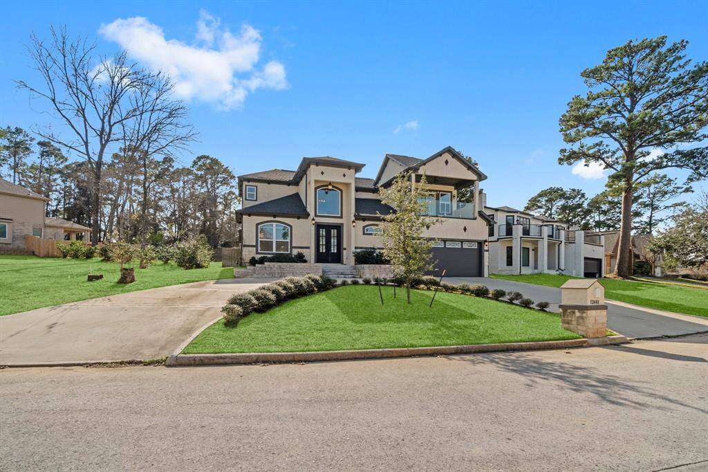 It features a large driveway, contemporary architectural design, and is situated in a neighborhood with mature trees.