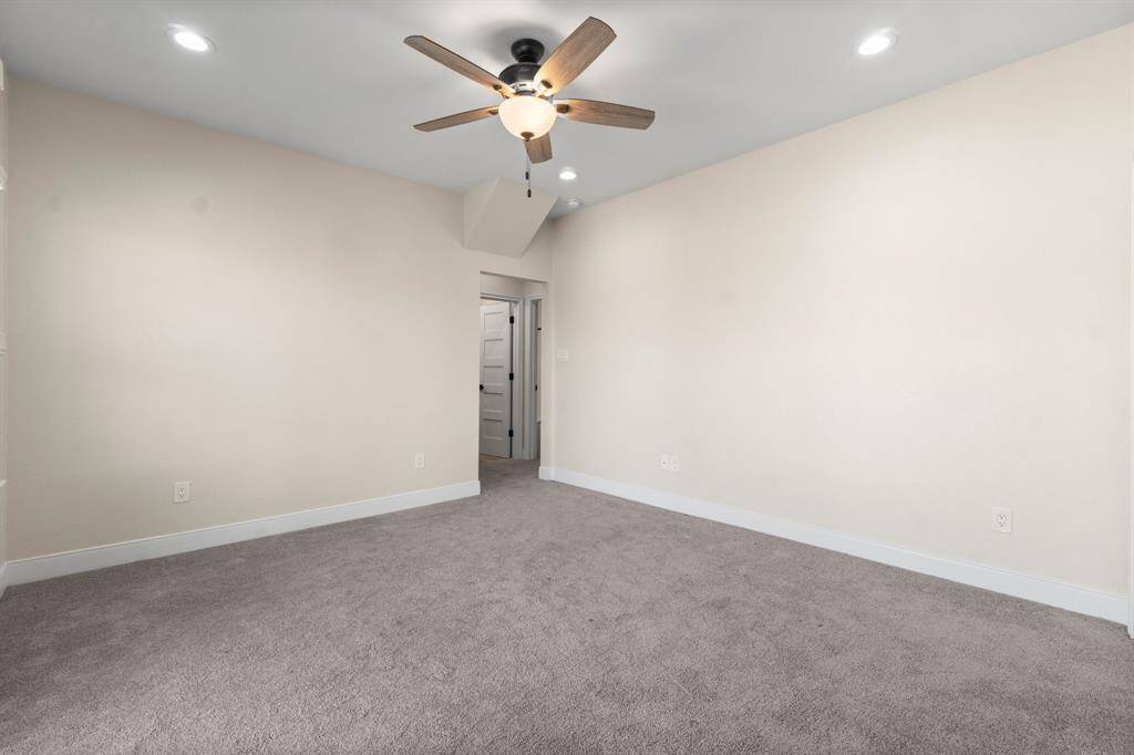 This room features neutral walls, plush carpeting, and a ceiling fan with recessed lighting. It has a cozy atmosphere and a doorway leading to an adjoining space, ideal for a bedroom or office.