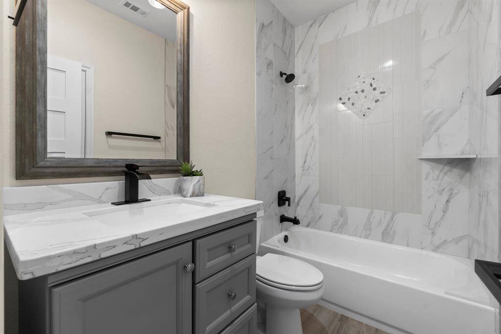 Modern bathroom with a sleek design featuring a marble countertop, gray vanity, and a bathtub with elegant tile backsplash.