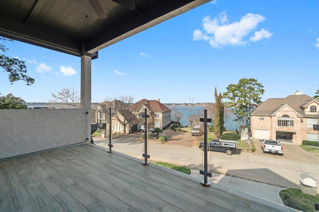 This photo showcases a spacious balcony with a stunning view of a lake and nearby houses. The setting is serene, featuring clear skies and an open layout, perfect for enjoying the scenic surroundings.
