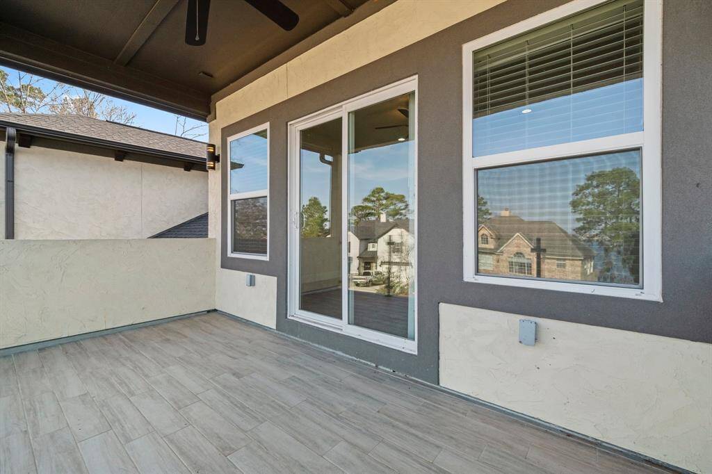 This photo shows a spacious, covered balcony with light wood-style flooring and large windows offering a view of the neighborhood. It's an inviting outdoor space perfect for relaxation or entertaining.