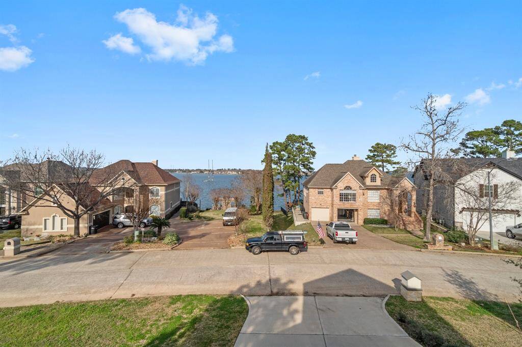 This photo showcases a quiet residential street with beautiful two-story homes. The properties have driveways and are framed by trees, offering a serene view of a nearby lake in the background.