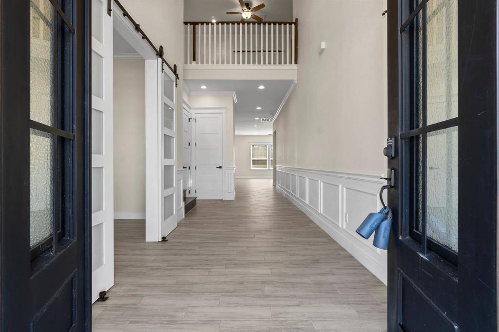 This photo showcases a spacious, bright entryway with wood-look flooring, high ceilings, and elegant wainscoting. It features a loft area with railing, modern sliding doors, and a long hallway leading to more rooms, creating a welcoming and open atmosphere.