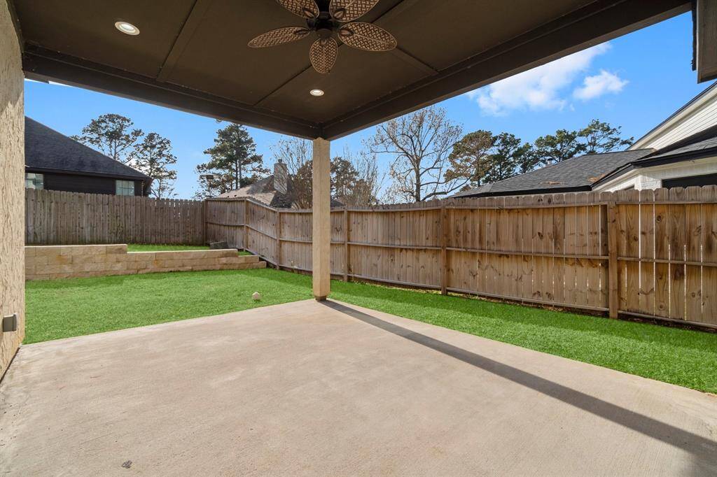 This photo showcases a covered patio with a ceiling fan, overlooking a fenced backyard. There's a stone retaining wall, providing a low-maintenance outdoor space. Ideal for relaxing and entertaining.