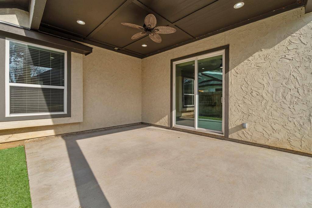 This photo features a spacious covered patio with a ceiling fan, recessed lighting, and a sliding glass door leading indoors. It has textured walls, making it ideal for outdoor relaxation or entertaining.