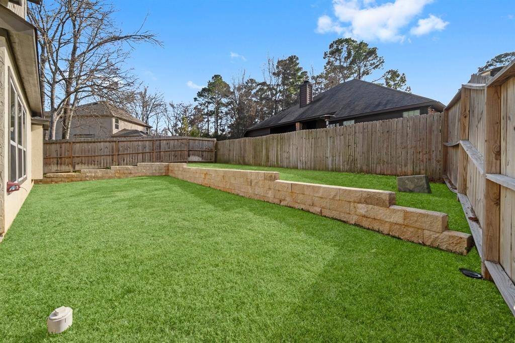 A spacious backyard featuring lush green grass and a tiered retaining wall, providing privacy with wooden fencing. Ideal for outdoor activities and relaxation.