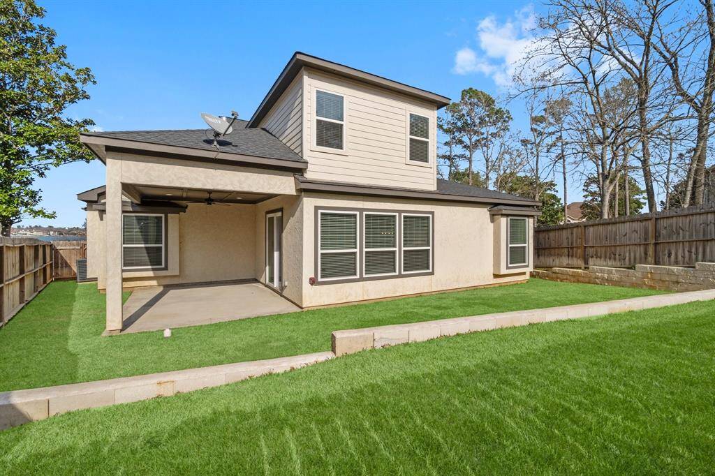 This photo showcases the backyard of a home featuring a well-maintained lawn, a covered patio area perfect for outdoor relaxation, and a two-story structure with multiple windows. The yard is enclosed with a wooden fence, providing privacy and a sense of security, surrounded by mature trees.