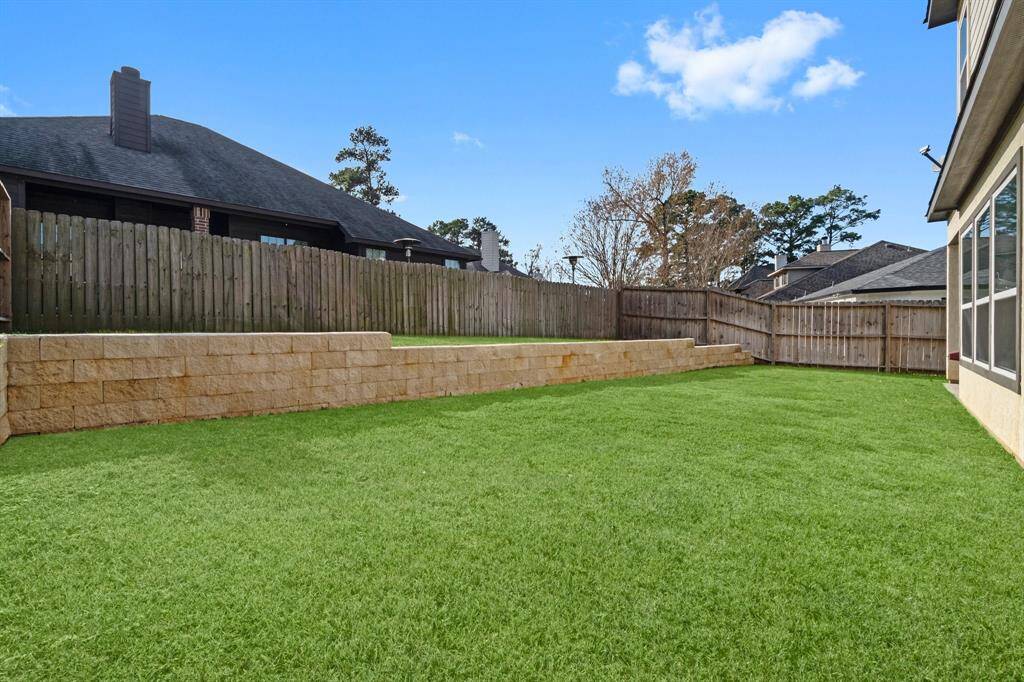 The photo showcases a spacious backyard with well-maintained green grass, a wooden privacy fence, and a stone retaining wall, perfect for outdoor activities and relaxation.