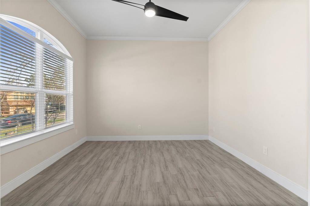 This room features light wood flooring, neutral-colored walls, a large arched window for ample natural light, and a modern ceiling fan. Perfect for a cozy office or guest room.