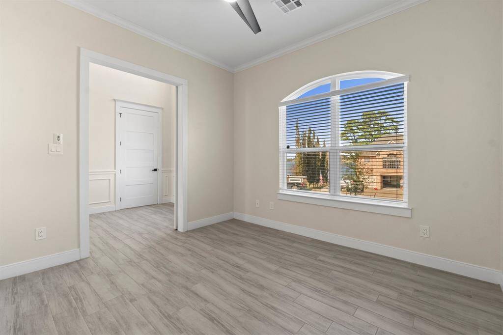 light wood flooring and neutral walls, creating a bright and inviting space. A large arched window with blinds offers ample natural light and a view of the neighborhood.