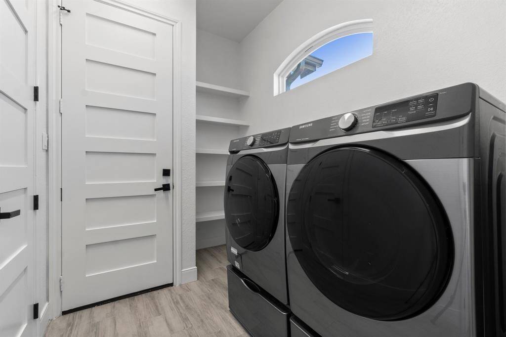 This photo shows a modern laundry room featuring a sleek washer and dryer set, built-in shelving, and a small window for natural light. The room has clean lines and a neutral color palette, providing a functional and stylish space.