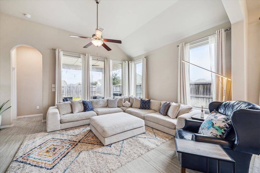 Bright and inviting living room featuring high ceilings and large windows that let in plenty of natural light. It includes a ceiling fan and views of the backyard offering a comfortable space for relaxation.