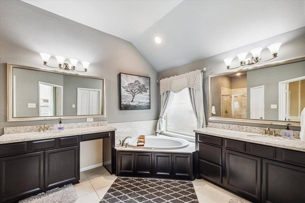The Primary bathroom features a spacious layout with dual vanities, elegant dark wood cabinetry, and granite countertops. It includes a luxurious soaking tub beneath a large window and a separate shower area. The room is well-lit with modern fixtures and has a neutral color palette for a serene ambiance.
