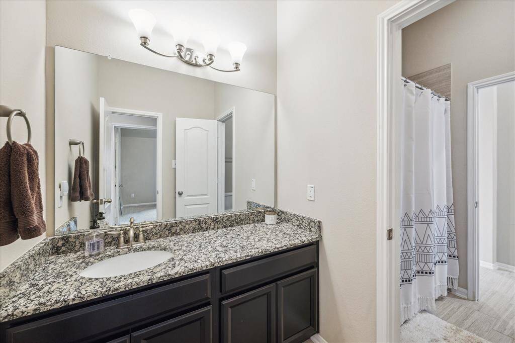 The guest bathroom features a granite countertop with an undermount sink and dark cabinetry. It includes a large mirror, modern light fixtures, and a separate shower area.