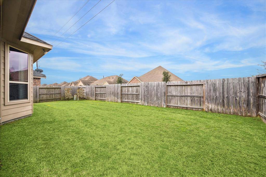 The spacious, fully fenced backyard with well-maintained grass, ideal for outdoor activities or gardening. The area offers privacy and a clear view of a bright blue sky from the corner lot location.