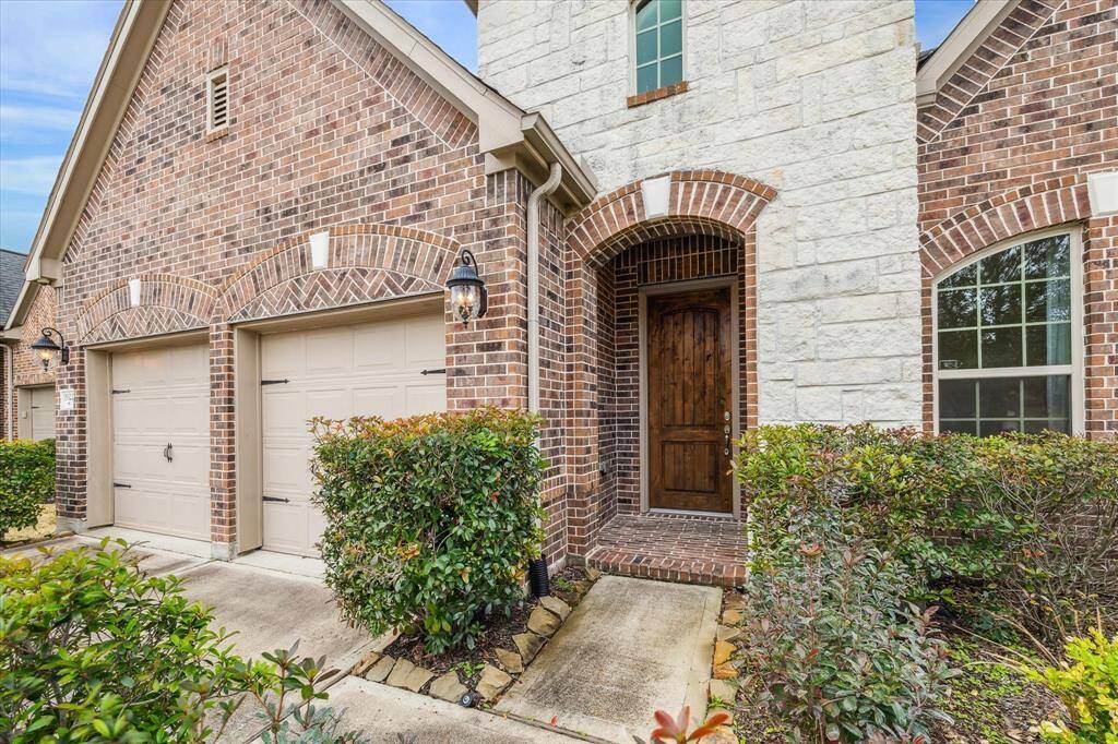 Welcoming front entry with a stone accent, a wooden front door, well-maintained landscaping and lantern-style lighting.