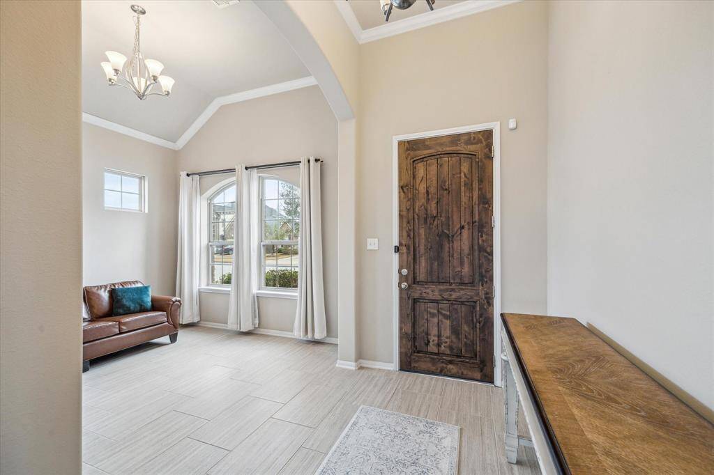 This entryway features a wooden door, light tiled upgraded flooring, and neutral walls. A bright sitting living area off the entry creates an inviting atmosphere. A small chandelier adds a touch of sophistication.