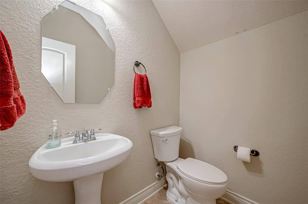 This is a compact, well-maintained half bathroom featuring a pedestal sink, toilet, and an octagonal mirror. It is accented with red towels and has a neutral color scheme.