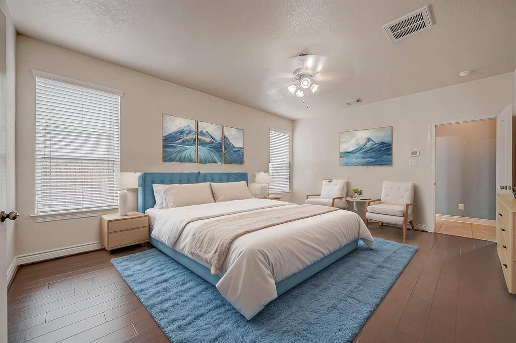 This is a spacious, well-lit primary bedroom featuring polished hardwood floors, neutral wall colors, and a ceiling fan with lighting. The room includes multiple doors and a window, providing both natural light and access to other parts of the home.(Virtual Stage)