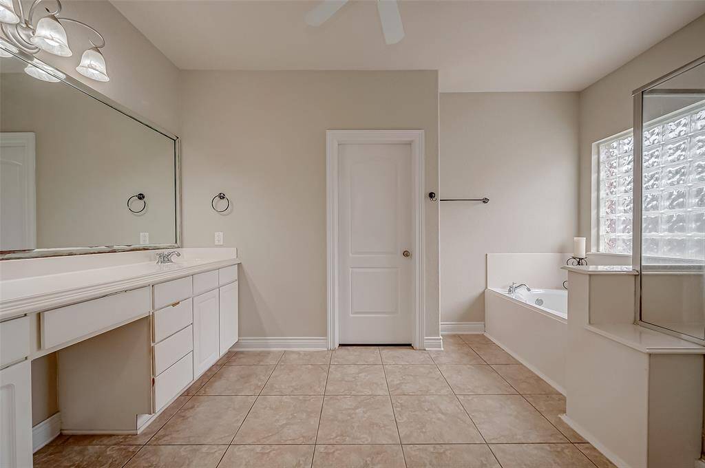 This is a spacious primary bathroom featuring a double vanity with ample storage, a large mirror, a separate tub, and a glass block window that provides natural light and privacy.
