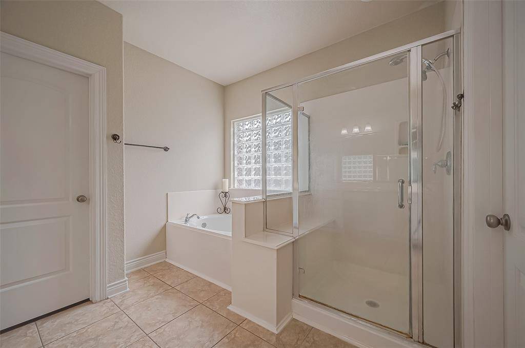 This is a spacious, LED-lit bathroom featuring a large tub, separate glass-enclosed shower, tiled flooring, and a frosted window for privacy and natural light.