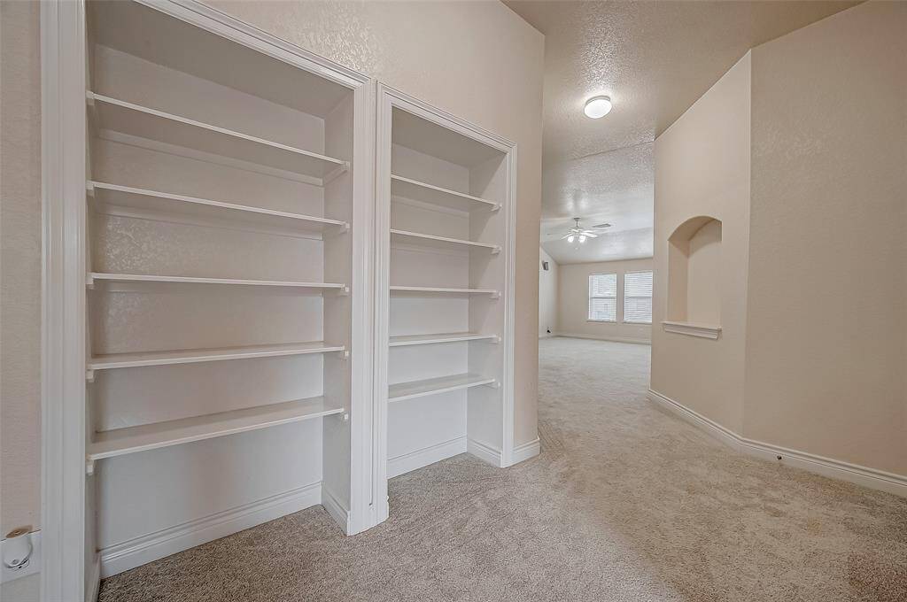 This is a spacious hallway with upgraded carpeting throughout the upstairs (installed in 2022) and featuring built-in white shelving units, perfect for storage or display. The area is LED-lit with ceiling lights and opens to an expansive game room space visible in the background.