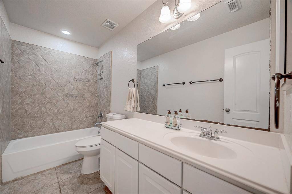 This is a well-maintained bathroom, located to the right of the game room, features a large vanity with ample storage, a full-sized bathtub with a tiled surround, and a separate toilet area. The space is bright, with modern LED lighting fixtures and a large mirror above the sink.