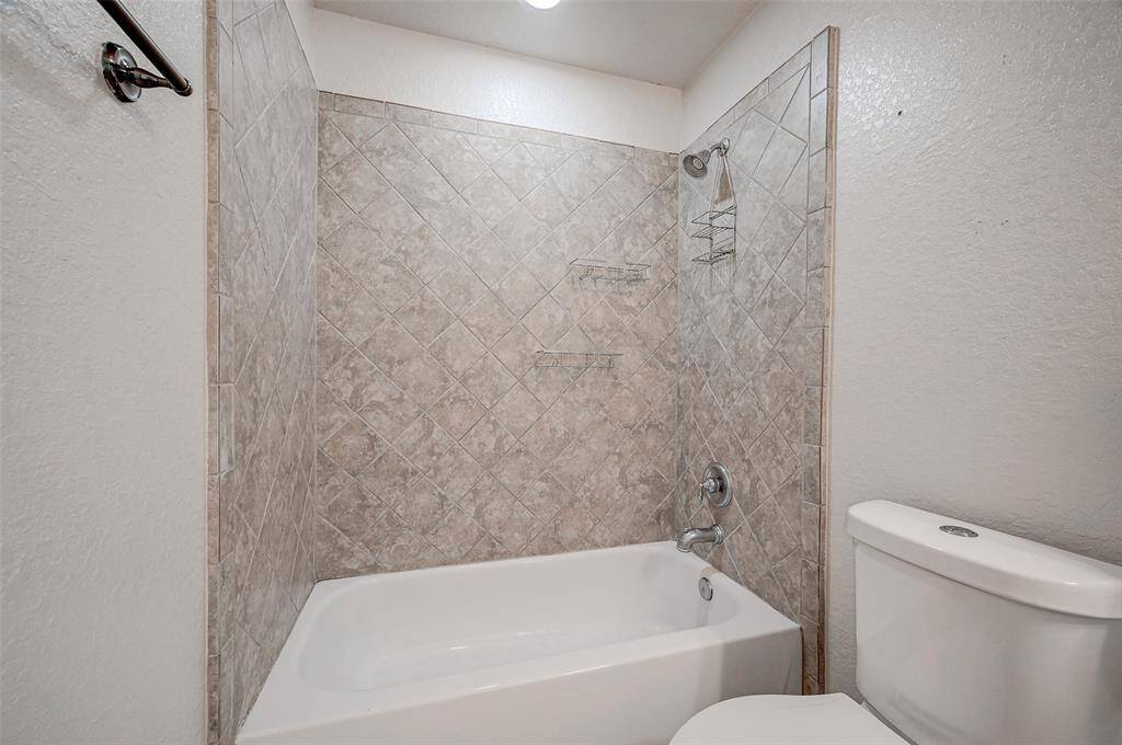 This secondary bathroom, located to the right of the game room, features a full tub with a diamond-patterned tile surround, a single showerhead. The space offers amble cabinetry storage for everyone's bathroom toiletries and personal care items.