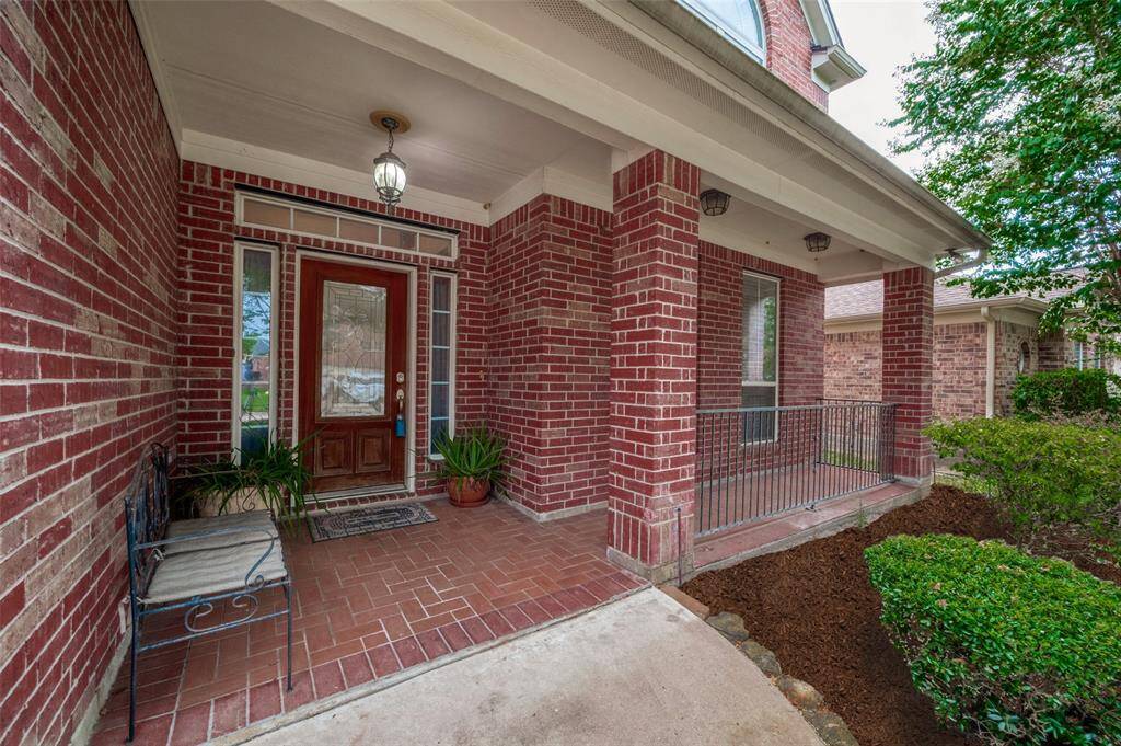 This is a welcoming brick house front porch with a classic wooden door, sidelights, a sitting bench, and mature landscaping.