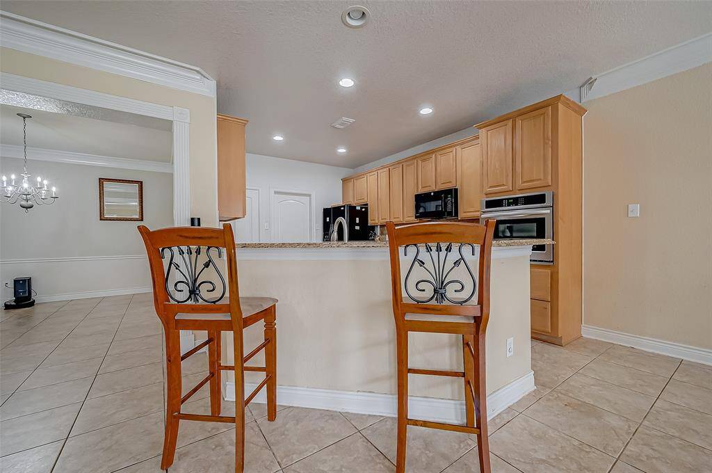 This is a spacious, well-lit kitchen with ample cabinetry, modern appliances, a bar seating area, and tile flooring, overlooking a formal dining, breakfast area and living spaces offers clear open sightlines in every direction.  Keep watch on the entire downstairs space with ease in this floor plan.
