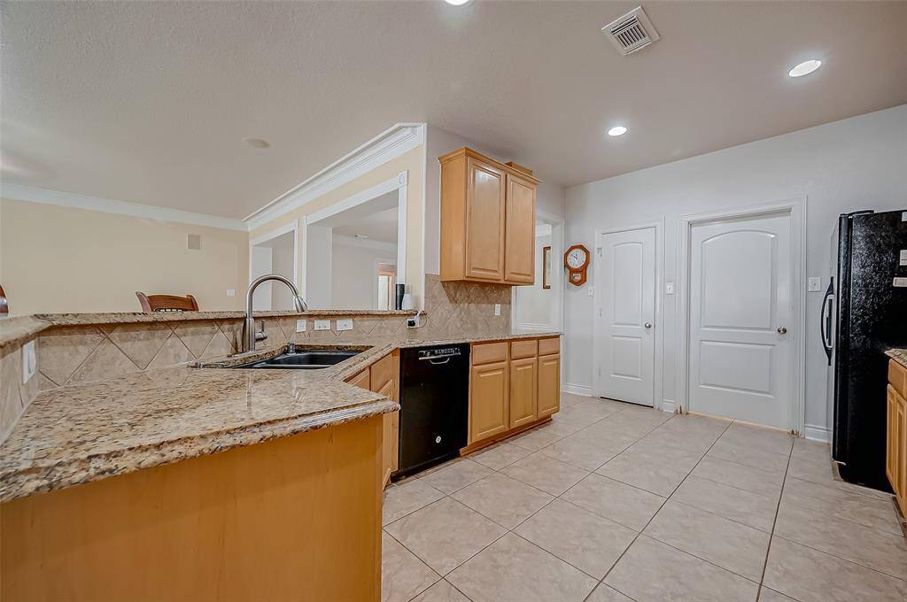 This is a spacious kitchen featuring granite countertops, wood cabinetry, modern appliances, and tiled flooring throughout is a chef's dream. It has ample LED recessed lighting and a pass-through window to an adjacent room enhancing the open feel and sightlines.