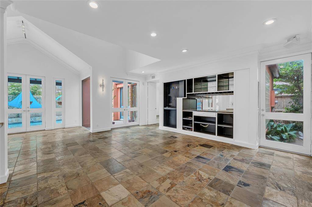 The family room is bright from all the windows and features high ceilings, tile floors, built-in shelving, and multiple doors leading to the homes outdoor spaces.