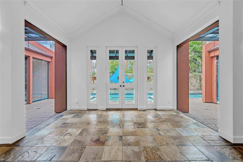 The dining room features a high vaulted ceiling, natural stone flooring, and French doors that provide direct access to an outdoor patio and pool.