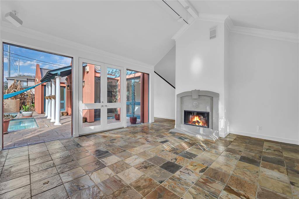 Bright, airy formal living room featuring a stone fireplace, high ceilings, and glass doors that lead to an inviting outdoor patio with a pool.