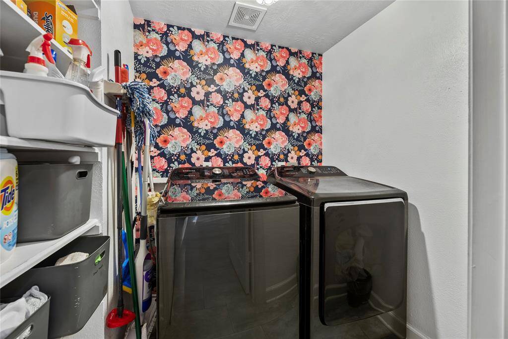 This charming utility room, conveniently located near the primary suite, offers washer and electric dryer connections, designer wallpaper, and tons of shelving for household items.