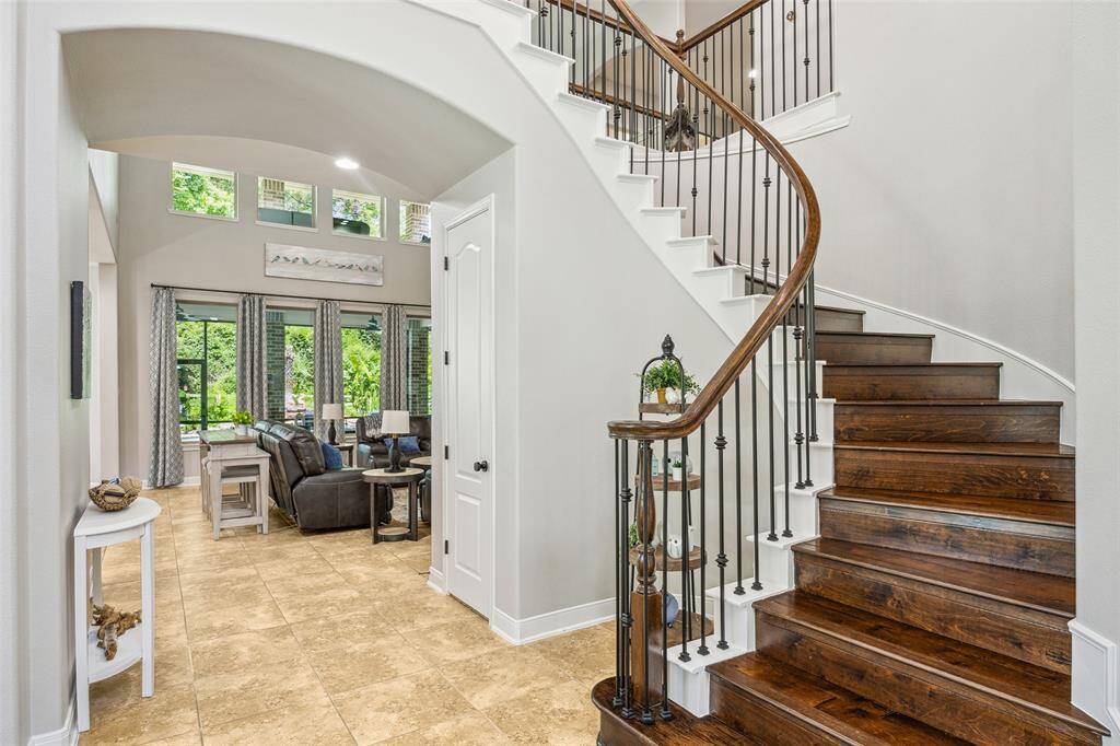 Step into sophistication with this grand entryway featuring a sweeping staircase with rich wooden steps and elegant iron railings, complemented by soaring ceilings and abundant natural light.