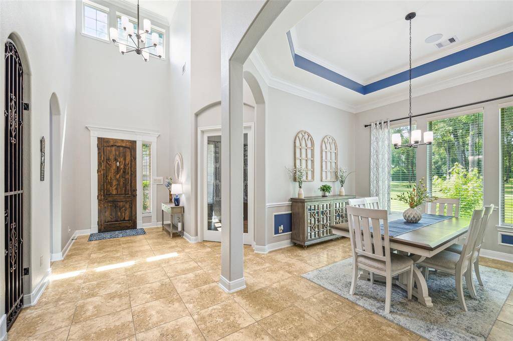 A bright, elegant formal dining area with tray ceiling, large windows, adjacent entryway to the kitchen.