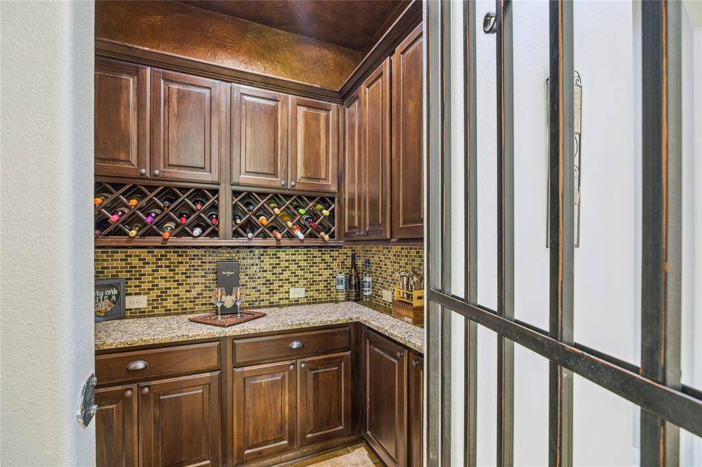 Discover an elegant wine sanctuary featuring a stunning mosaic backsplash and sleek granite countertops, framed by an ornate wrought iron door.