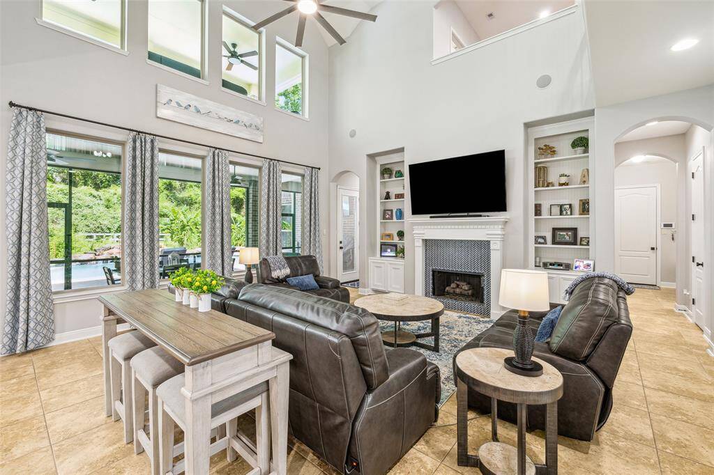 A spacious, high-ceiling living room with built-ins, large windows, a gas fireplace, surround sound, overlooking the pool area.