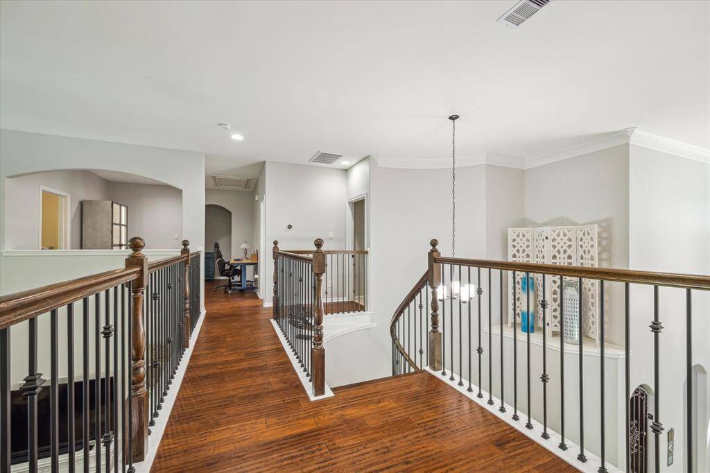 Spacious, well-lit hallway with wooden floors, and dark iron balustrades overlooking an interior space
