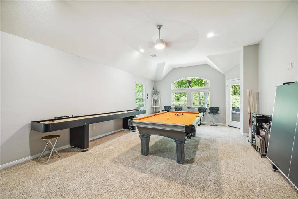 Spacious gameroom with beige carpet, vaulted ceiling, large window, door to outside patio