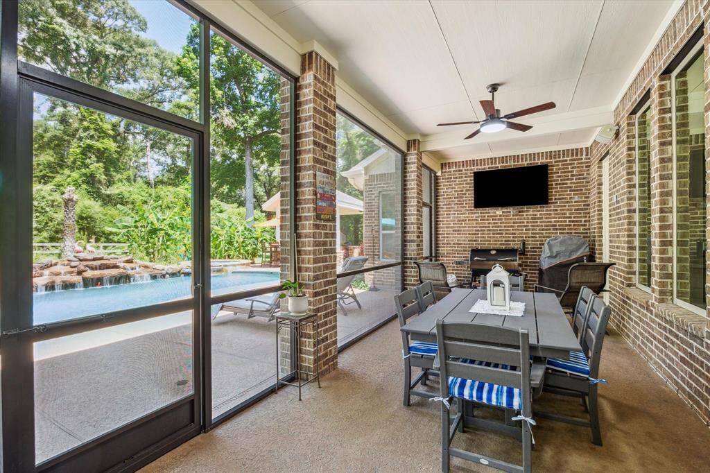 Screened in covered patio with ceiling fan, overlooking pool with a rock waterfall surrounded by trees