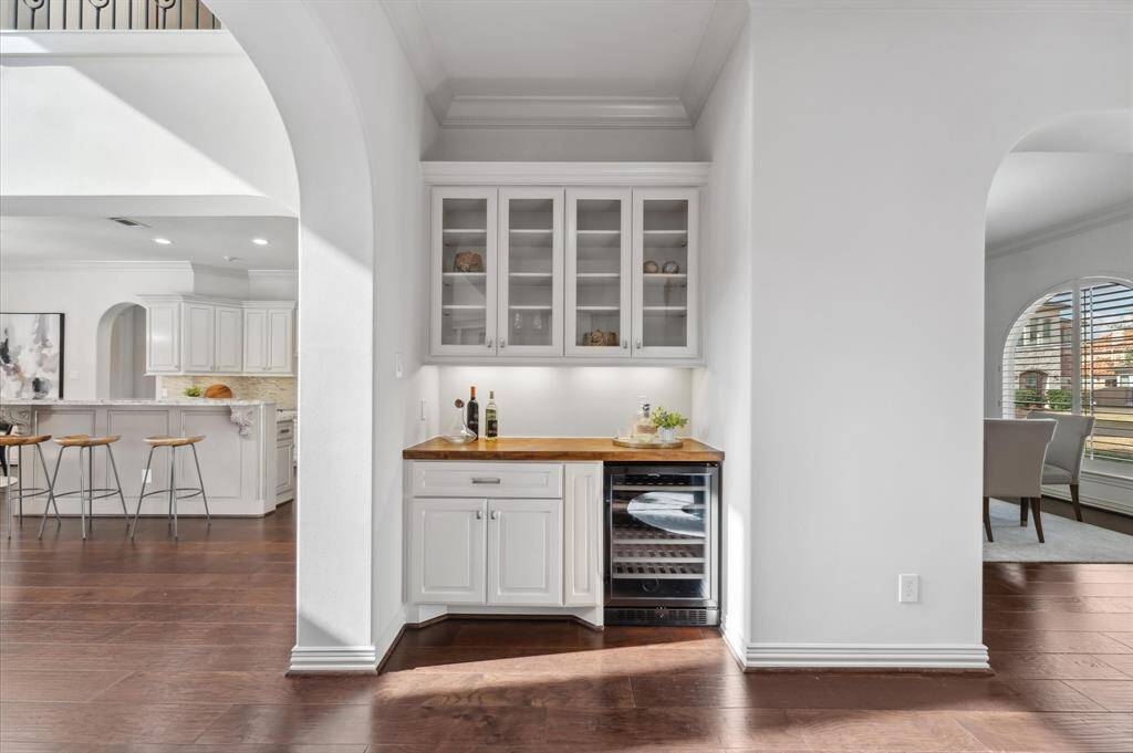 Dry bar with modern white cabinetry, and a built-in wine cooler. The space is inviting with an adjacent dining area and a view into a spacious living area, ideal for entertaining.